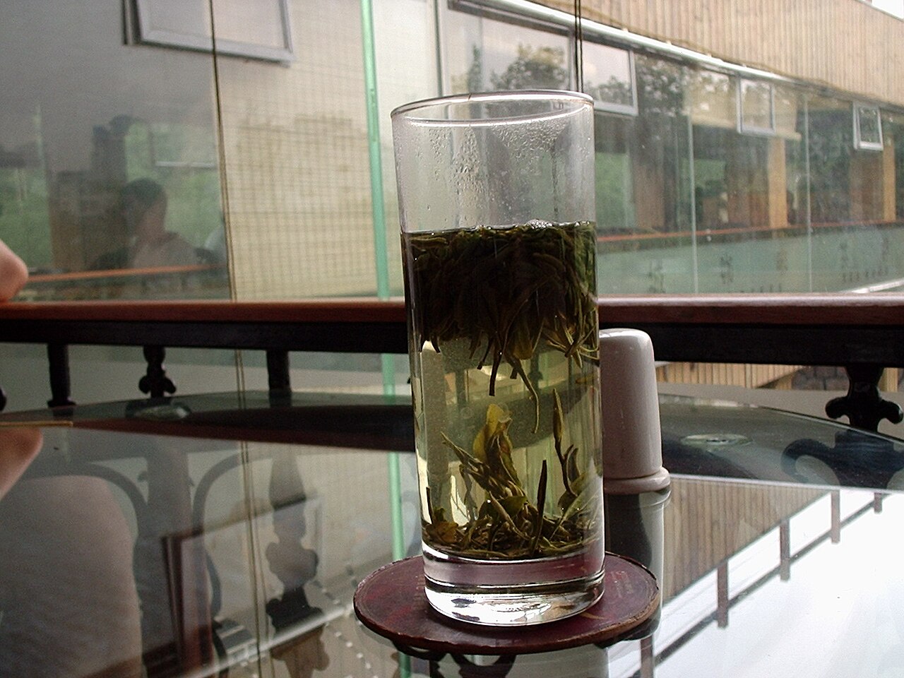 Pale tea leaves opening in a glass, used as a visual cue for white tea leaf integrity and fresh early-stage character